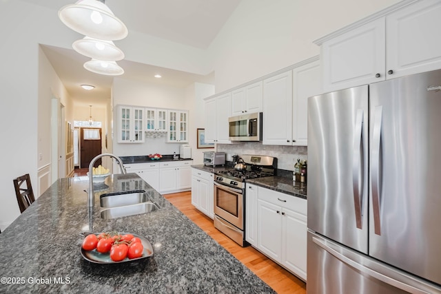 kitchen with light wood finished floors, glass insert cabinets, white cabinets, stainless steel appliances, and a sink