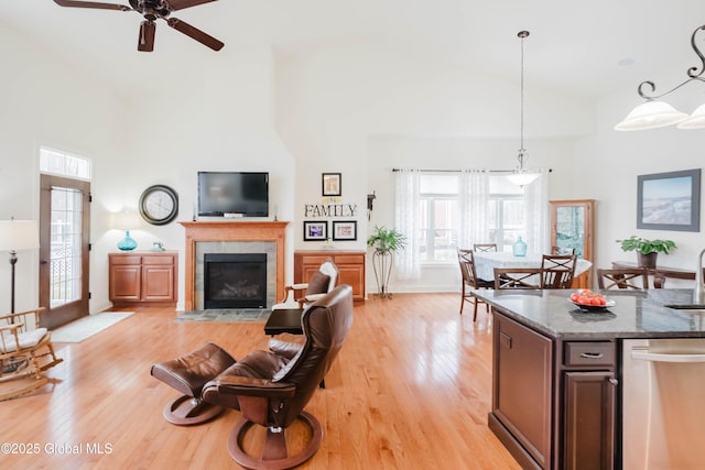 living room with light wood-type flooring, high vaulted ceiling, ceiling fan, and a tile fireplace