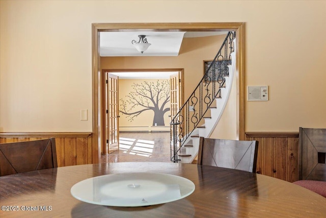 dining area featuring a baseboard heating unit, a wainscoted wall, wood walls, and stairway