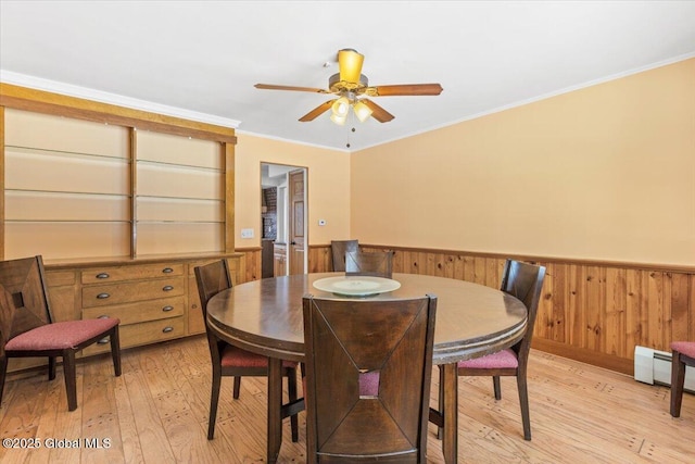 dining area featuring light wood-style flooring, wood walls, ornamental molding, baseboard heating, and wainscoting