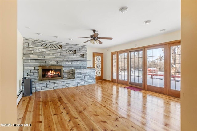 unfurnished living room with ceiling fan, a fireplace, wood-type flooring, and a baseboard radiator