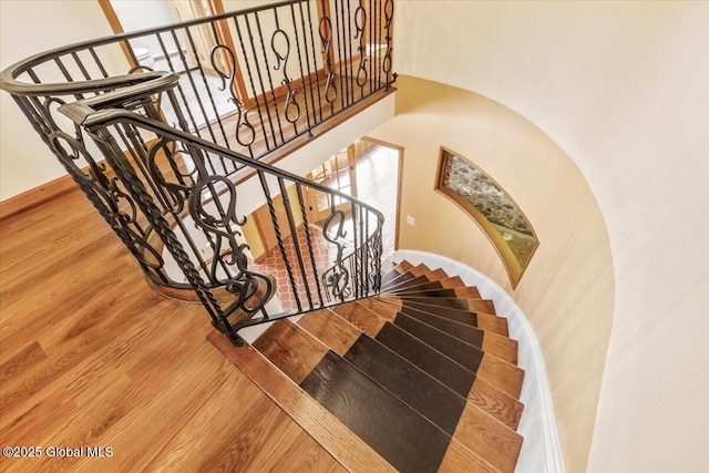 stairway featuring a high ceiling, baseboards, and wood finished floors