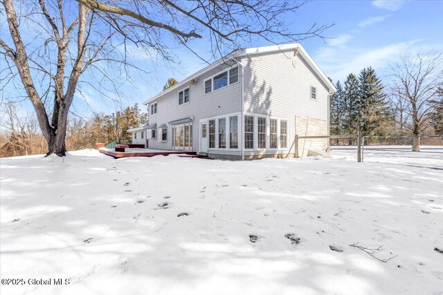 snow covered property featuring a garage, a sunroom, and a deck