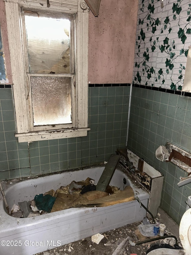 bathroom with tile walls, toilet, a tub to relax in, and wainscoting