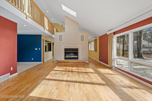 unfurnished living room featuring visible vents, wood finished floors, a high ceiling, a skylight, and baseboards