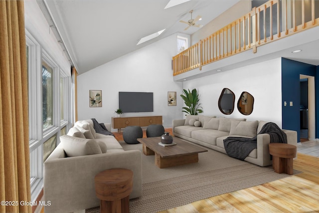 living room featuring a ceiling fan, a skylight, wood finished floors, and high vaulted ceiling