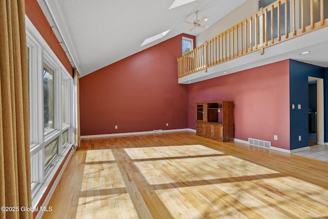 unfurnished living room featuring visible vents, baseboards, hardwood / wood-style floors, a skylight, and high vaulted ceiling