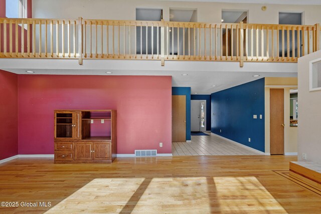 unfurnished living room featuring a high ceiling, wood finished floors, visible vents, and baseboards