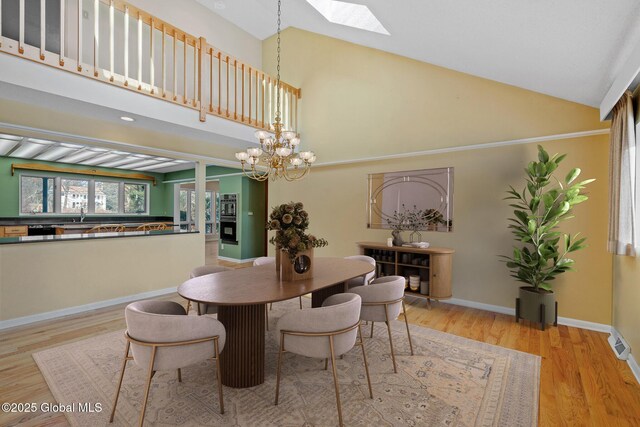 dining space featuring light wood finished floors, baseboards, a skylight, an inviting chandelier, and high vaulted ceiling