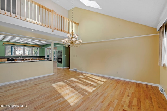 unfurnished living room featuring baseboards, high vaulted ceiling, an inviting chandelier, a skylight, and light wood-type flooring