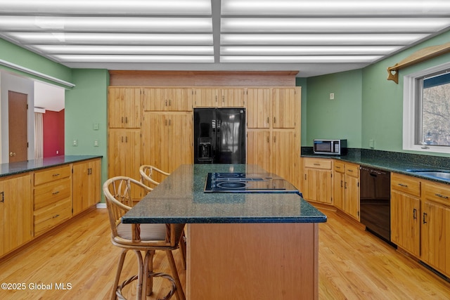 kitchen with light wood finished floors, a breakfast bar, a sink, black appliances, and a center island