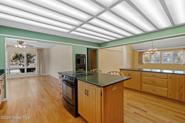 kitchen with pendant lighting, black appliances, light wood-style flooring, ceiling fan with notable chandelier, and a center island