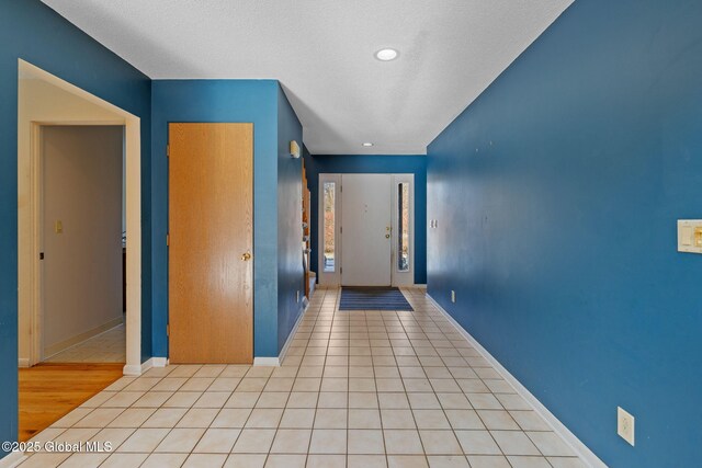 hallway with recessed lighting, baseboards, a textured ceiling, and light tile patterned flooring