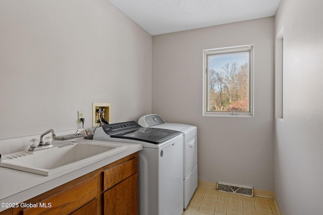 washroom with visible vents, baseboards, washer and clothes dryer, cabinet space, and a sink