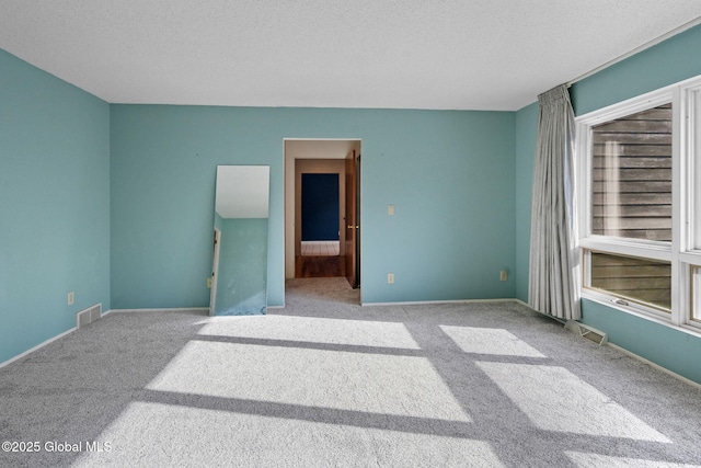 unfurnished room featuring carpet flooring, baseboards, visible vents, and a textured ceiling