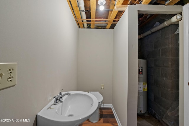 bathroom with water heater, concrete block wall, baseboards, and a sink