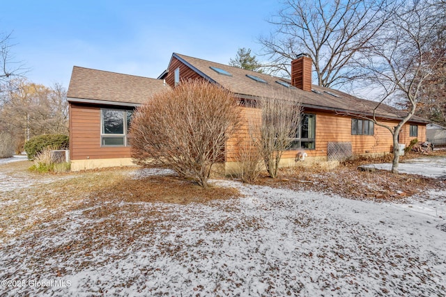 view of snowy exterior with roof with shingles and a chimney