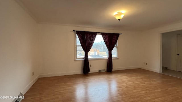 spare room with light wood-type flooring, visible vents, ornamental molding, and baseboards