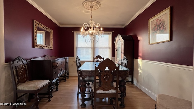 dining room featuring ornamental molding, light wood-type flooring, a wainscoted wall, and an inviting chandelier