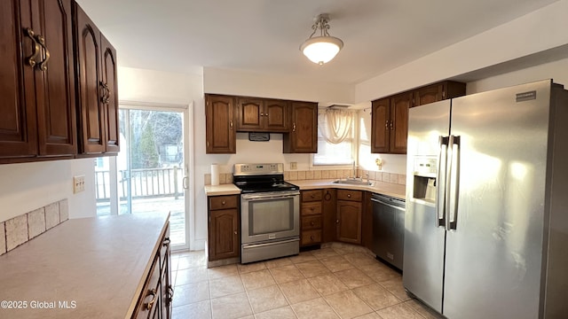 kitchen with light tile patterned floors, stainless steel appliances, dark brown cabinets, light countertops, and a sink