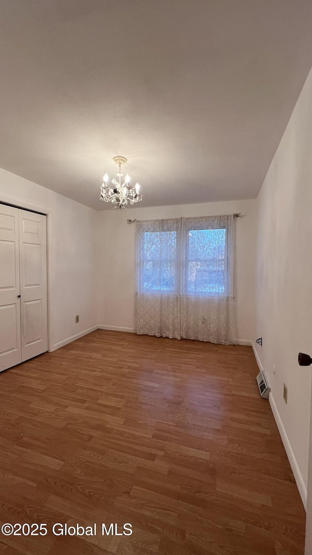 unfurnished room featuring a notable chandelier, baseboards, and wood finished floors