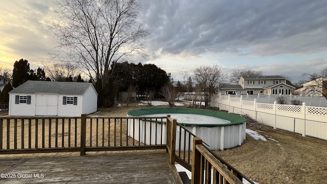 deck at dusk featuring a fenced in pool, a fenced backyard, an outdoor structure, and a storage shed