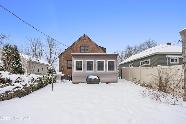 snow covered house featuring brick siding and fence