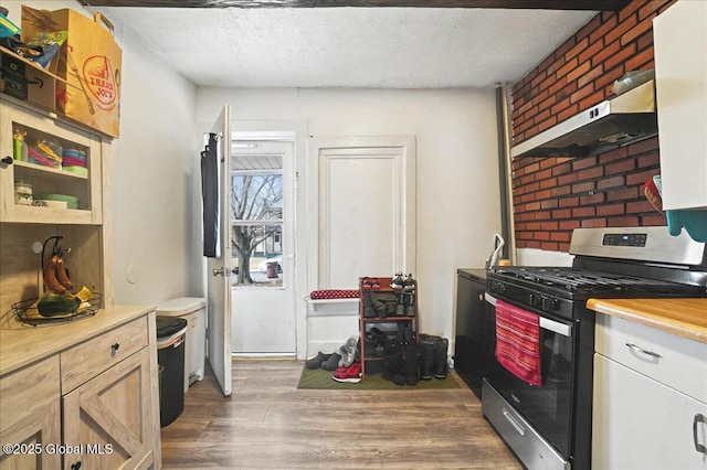 kitchen with wood finished floors, brick wall, under cabinet range hood, a textured ceiling, and gas range