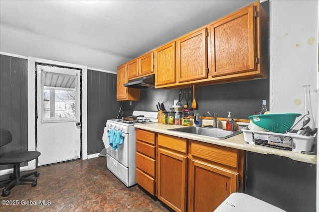kitchen featuring brown cabinetry, gas range gas stove, a sink, light countertops, and under cabinet range hood