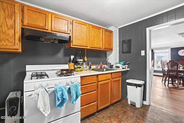 kitchen featuring gas range gas stove, a sink, light countertops, under cabinet range hood, and brown cabinets