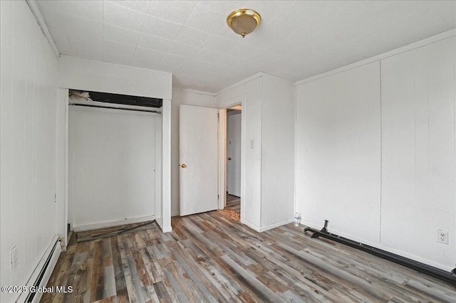 unfurnished bedroom featuring wood finished floors, a closet, and a baseboard radiator