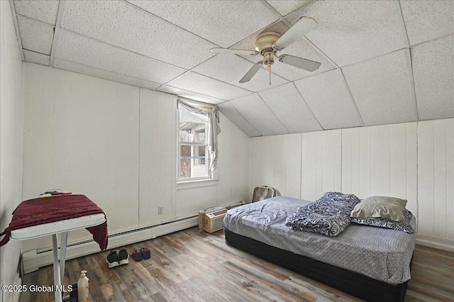 bedroom featuring a drop ceiling, wood finished floors, a baseboard radiator, ceiling fan, and vaulted ceiling