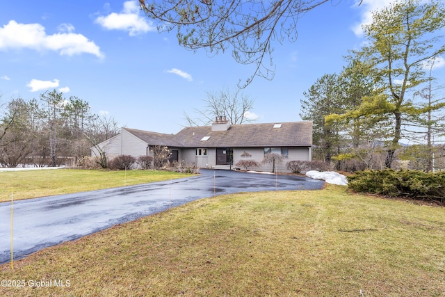 view of front of property with driveway, a chimney, and a front lawn