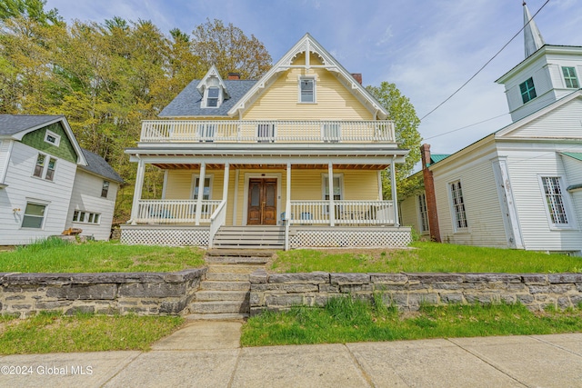 victorian house featuring a porch, a front yard, a chimney, and a balcony