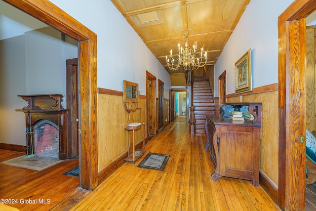 hall with hardwood / wood-style flooring, wooden walls, stairs, wainscoting, and an inviting chandelier