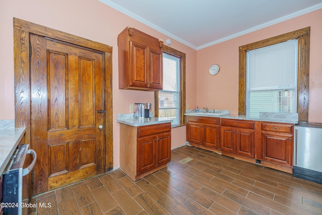 kitchen with wood finish floors, light countertops, ornamental molding, brown cabinetry, and a sink