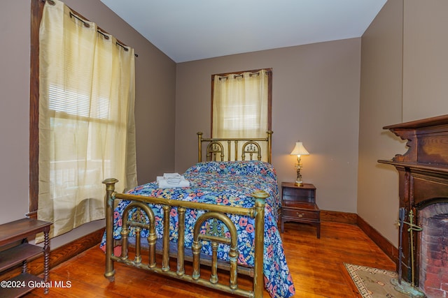 bedroom with a brick fireplace, wood finished floors, and baseboards