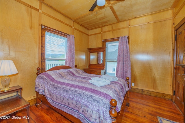 bedroom featuring a ceiling fan, wood walls, and hardwood / wood-style floors