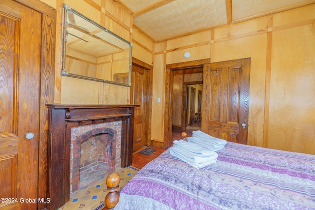 bedroom with a brick fireplace, wood finished floors, and wooden walls