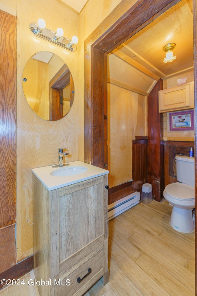 bathroom with lofted ceiling, toilet, a baseboard heating unit, wood finished floors, and vanity