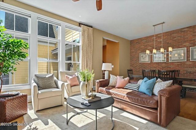 living area featuring ceiling fan with notable chandelier and brick wall