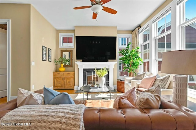 living room featuring a fireplace, baseboards, ceiling fan, and wood finished floors