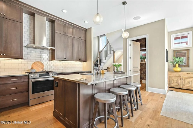 kitchen with gas range, dark brown cabinets, wall chimney exhaust hood, and light wood finished floors