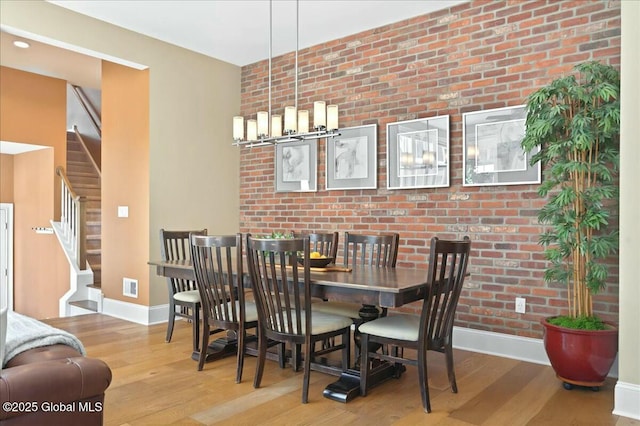 dining space featuring brick wall, stairs, baseboards, and wood finished floors