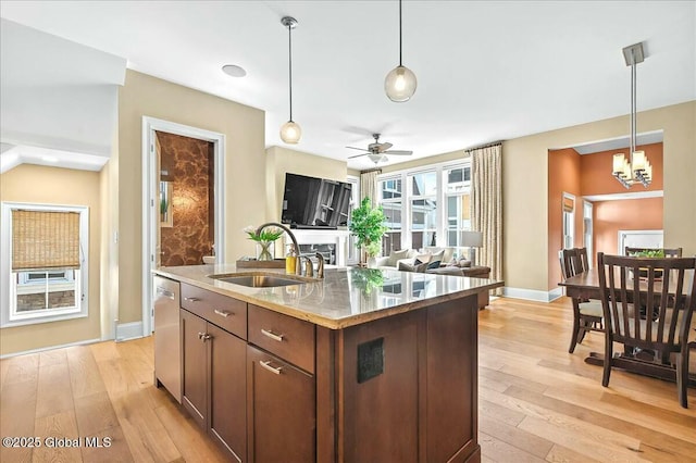 kitchen with a sink, decorative light fixtures, light stone counters, stainless steel dishwasher, and light wood finished floors