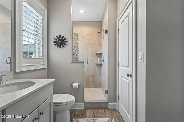 bathroom with toilet, wood finished floors, a shower stall, baseboards, and vanity