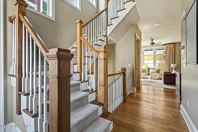 staircase featuring hardwood / wood-style floors, a high ceiling, baseboards, and ceiling fan