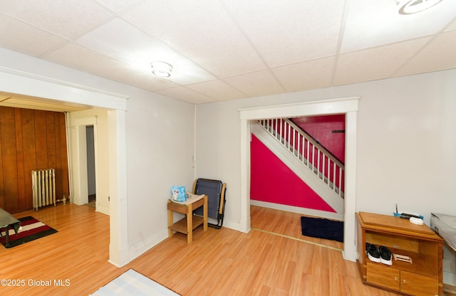 interior space featuring radiator, wood finished floors, baseboards, and a drop ceiling