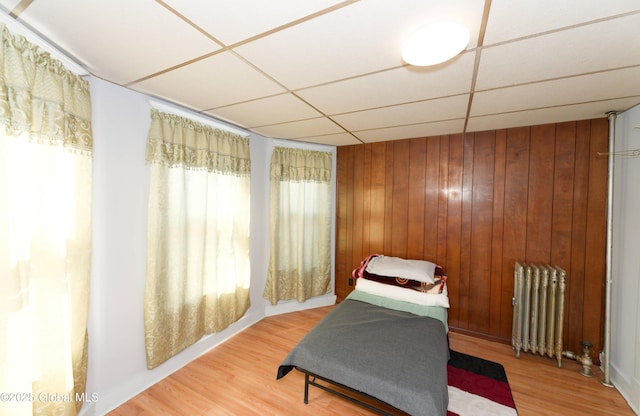 sitting room featuring a drop ceiling, radiator heating unit, wood finished floors, and wood walls