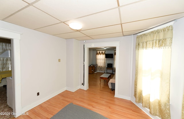 empty room featuring light wood finished floors, a drop ceiling, and baseboards